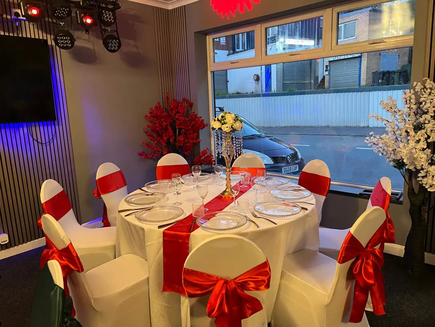 Gold Hall tables dressed with red runners and red chair bows beside the large windows, with the screen and stage lights behind