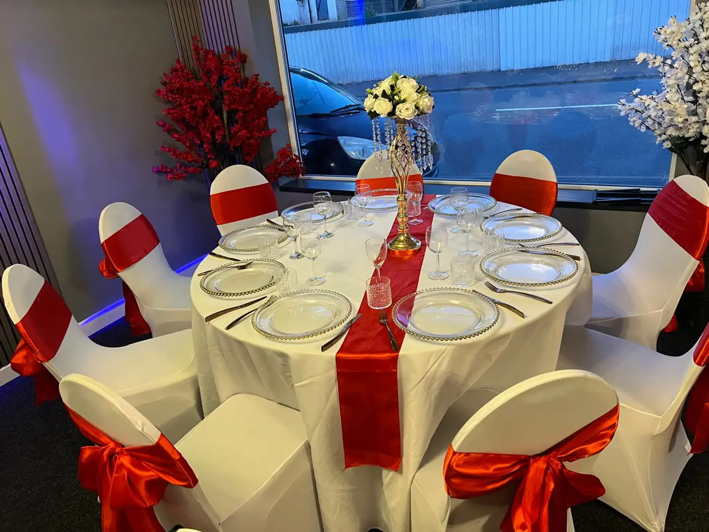 Banquet table with a red satin runner, red chair bows and a floral centrepiece by the windows