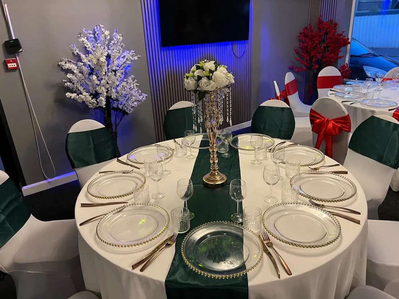 Banquet table with an emerald green runner and sashes, gold charger plates and a white floral centrepiece