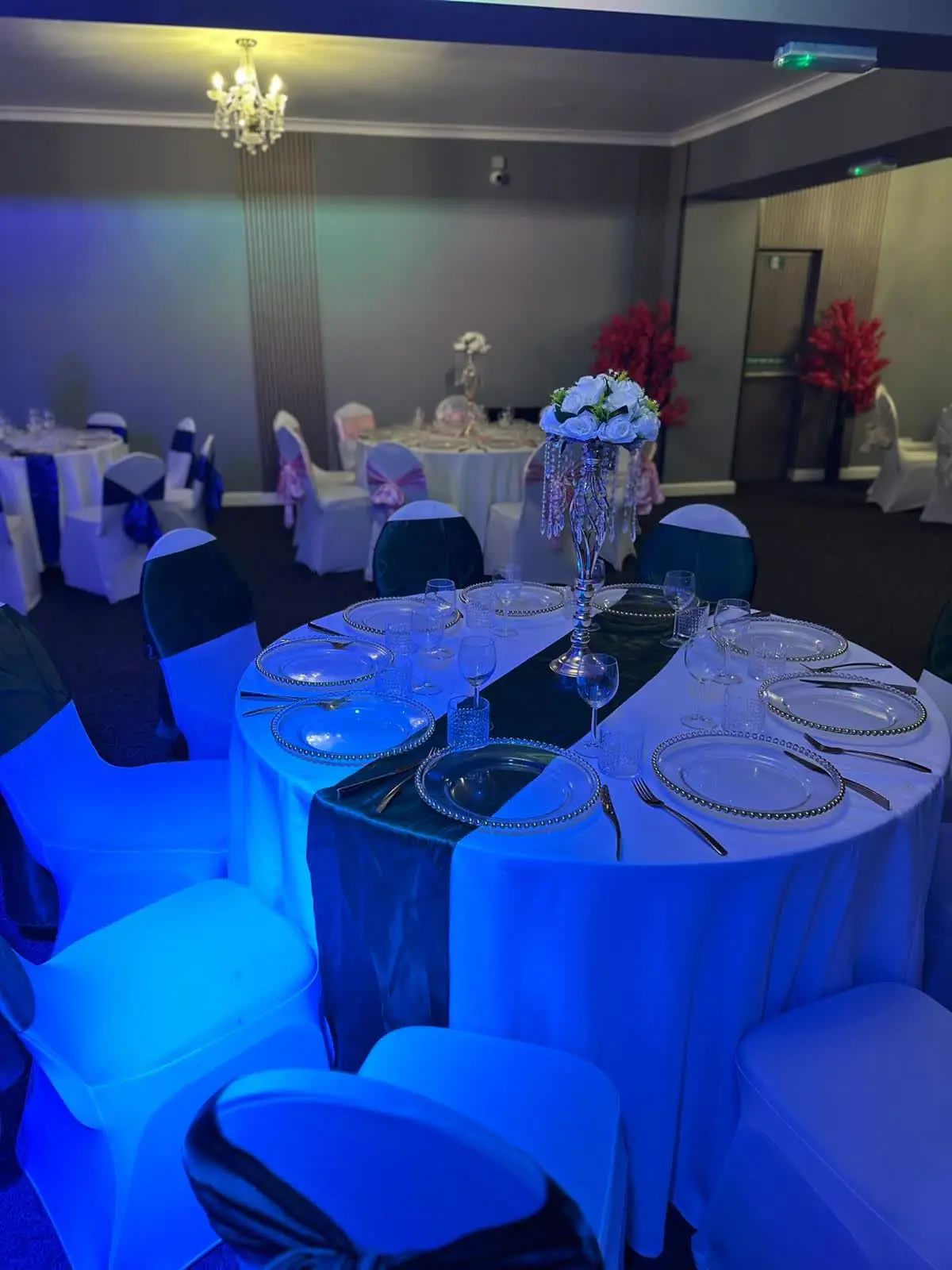 The Gold Hall at night, washed in deep blue light, with round tables set for dinner beneath a chandelier