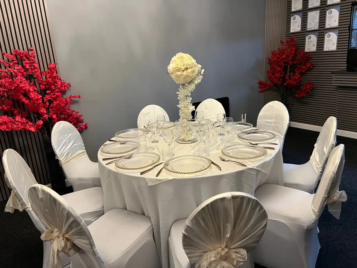 Round banquet table with ivory chair covers, gold-rimmed charger plates, crystal glassware and a cream rose centrepiece