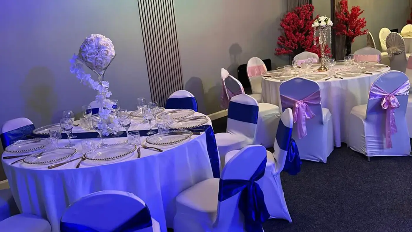 Tables in blue evening light with royal blue chair sashes, a lilac floral centrepiece and pink-tied chairs behind