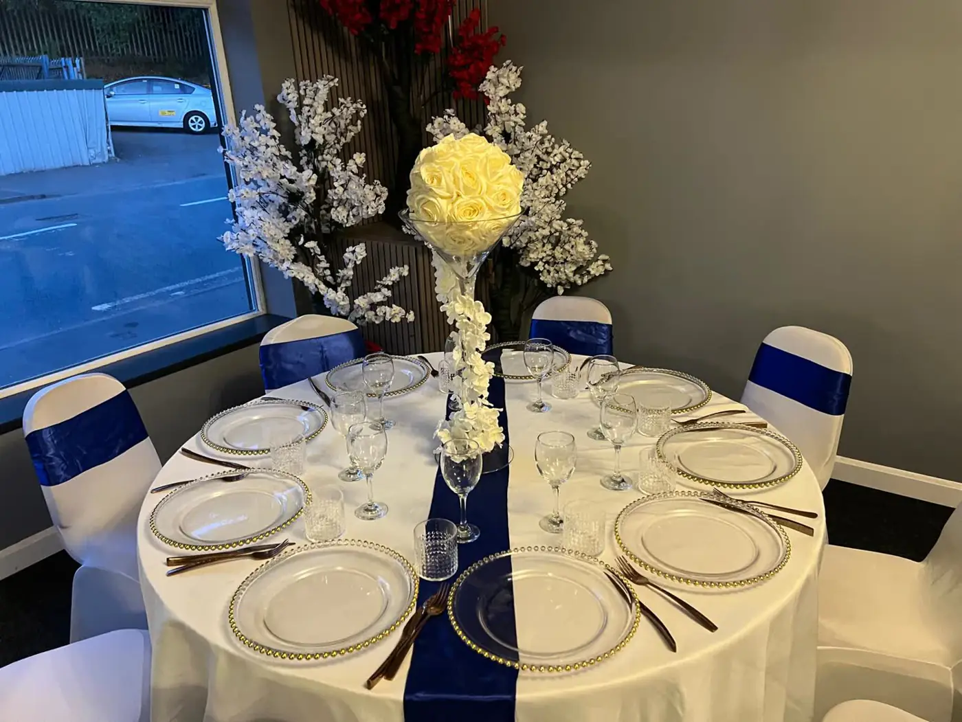 Banquet table with a navy runner, navy chair sashes and a tall white floral centrepiece