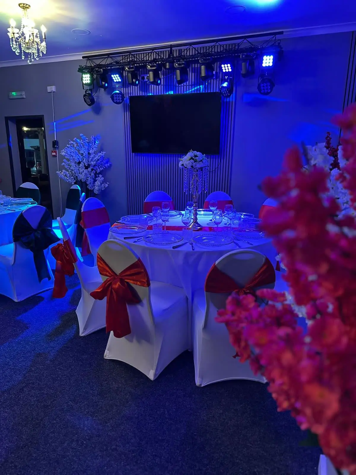 Silver Hall under coloured stage lighting, with white chair covers, red sashes and pink blossom trees