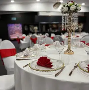 Table with red fan-folded napkins and a crystal floral centrepiece, with more tables laid behind