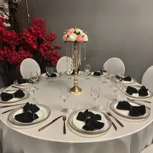 White table set with black folded napkins, beaded charger plates and a rose centrepiece