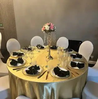 Round table with a gold satin cloth, black folded napkins and a pink floral centrepiece