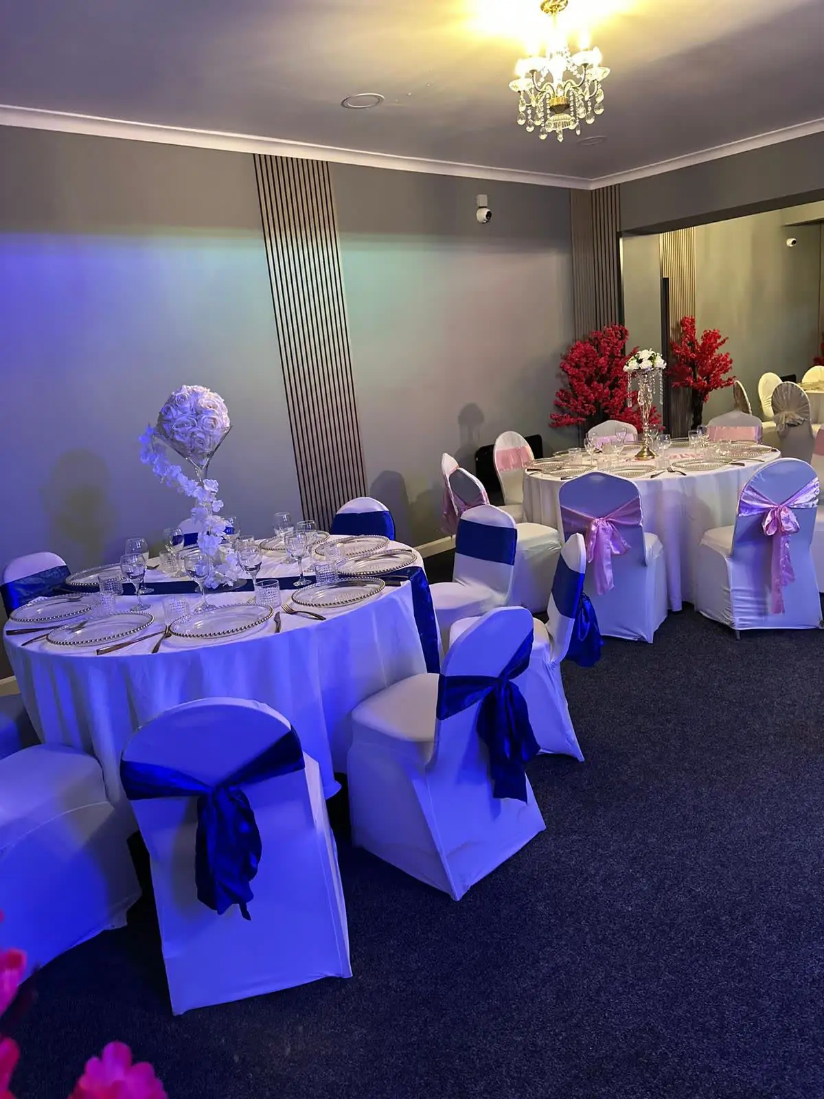 Gold Hall tables with white chair covers and navy sashes under blue mood lighting and a chandelier