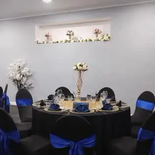 Table with a black cloth, black chair covers and royal blue sashes in a white-walled room