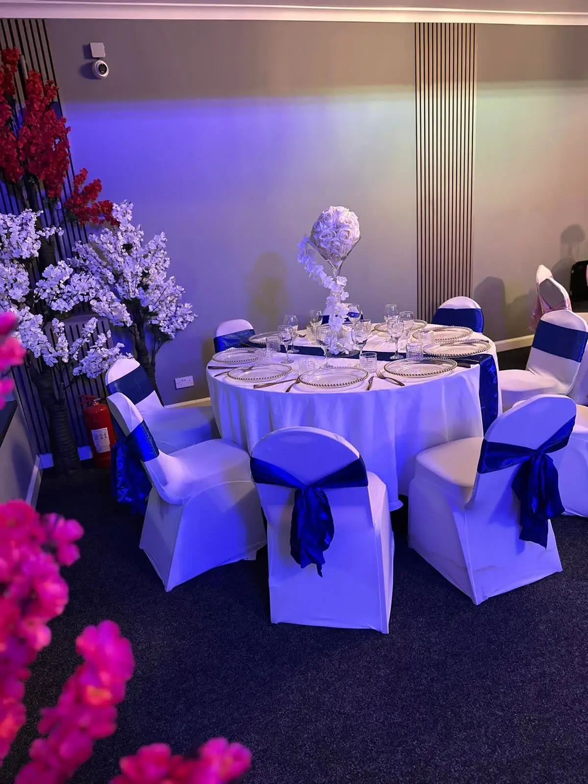 Silver Hall tables with white covers and navy sashes in soft pink and violet light, with pink blossom in the foreground